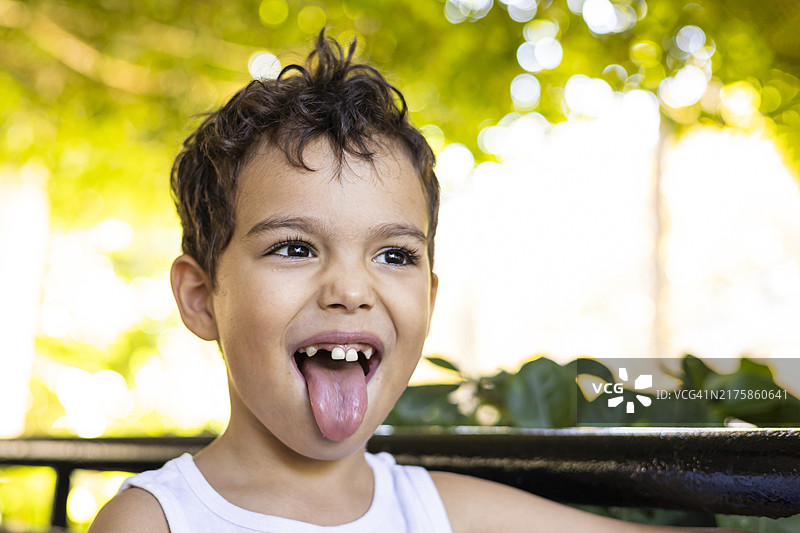 快乐的孩子在阳光明媚的公园里调皮地吐舌头图片素材