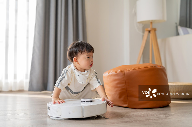 可爱的亚洲男婴好奇地研究扫地机器人图片素材