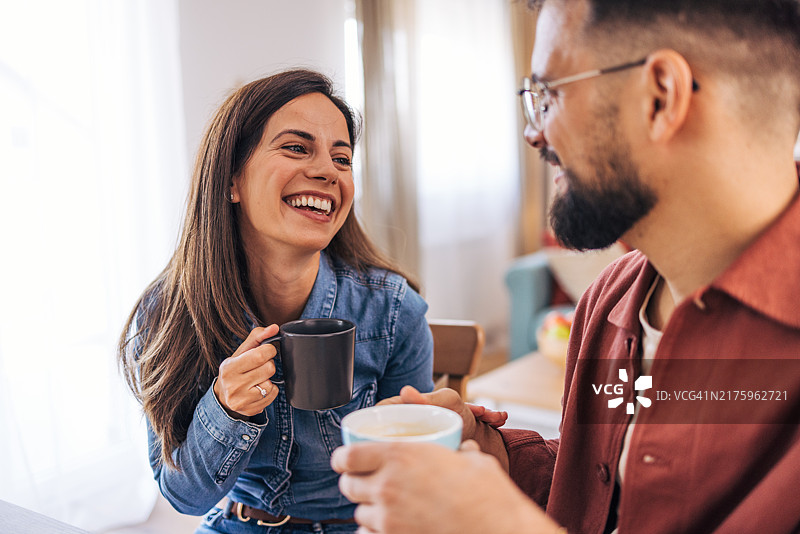 一对快乐的成年夫妇坐在客厅的桌旁，享受咖啡图片素材