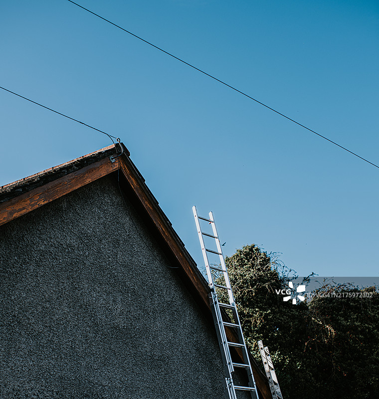 阳光明媚的下午，靠在房子上的梯子，准备进行屋顶维护工作图片素材