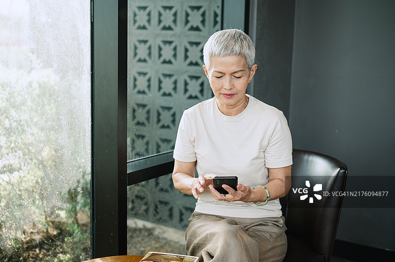 亚洲退休女士在咖啡店里坐着使用手机。图片素材