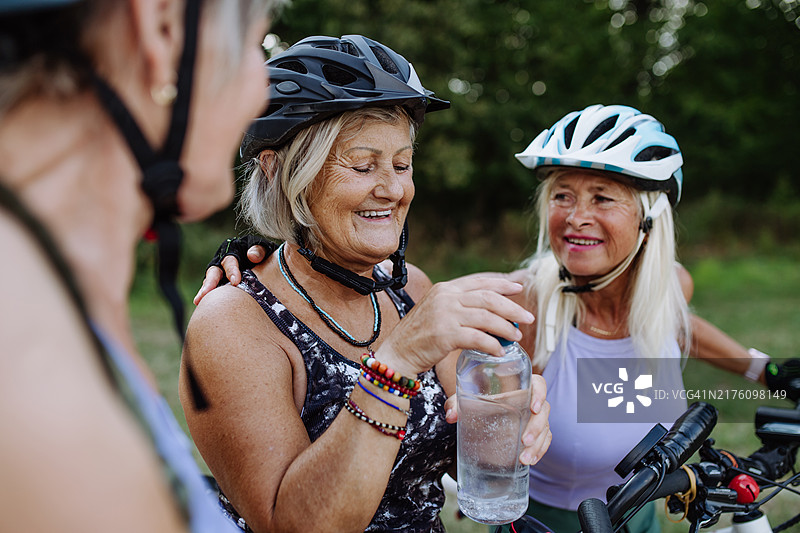 在自然中骑自行车旅行休息、喝水的三位老年朋友。骑电动自行车的年长女性图片素材