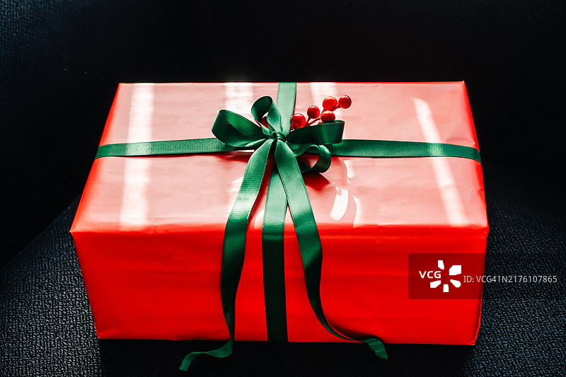 阳光下系着绿色丝带和红色浆果的红色圣诞礼盒图片素材