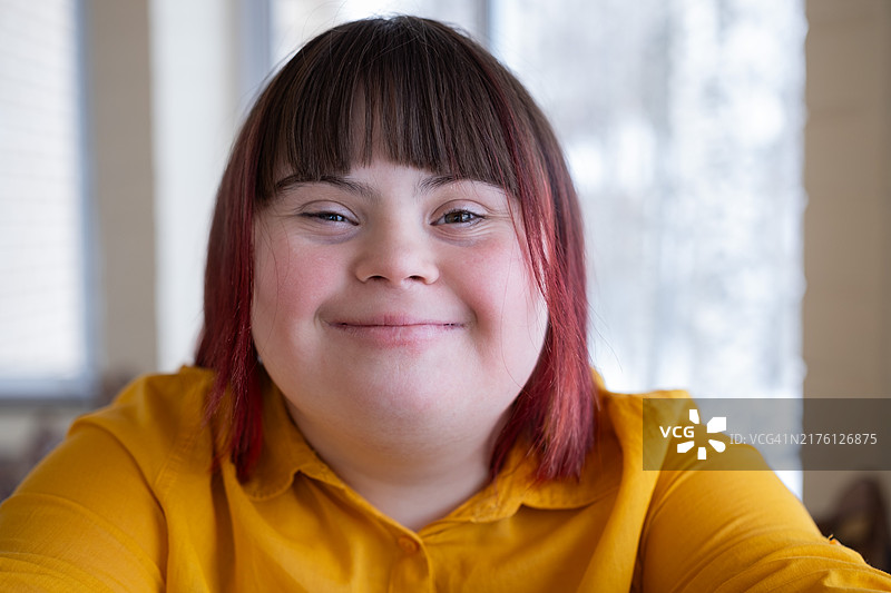 患有唐氏综合征的年轻女人在室内自拍，微笑，看着镜头图片素材