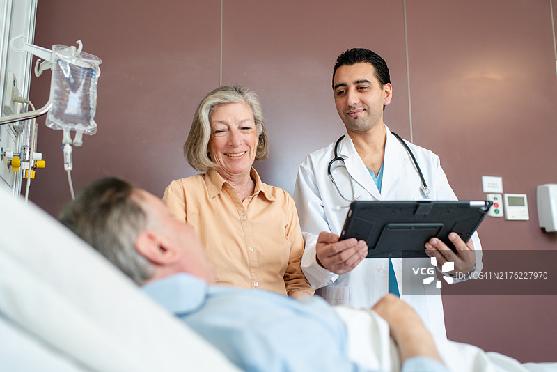 医生在医院病房检查躺在床上的老年患者，妻子在旁边站着。图片素材