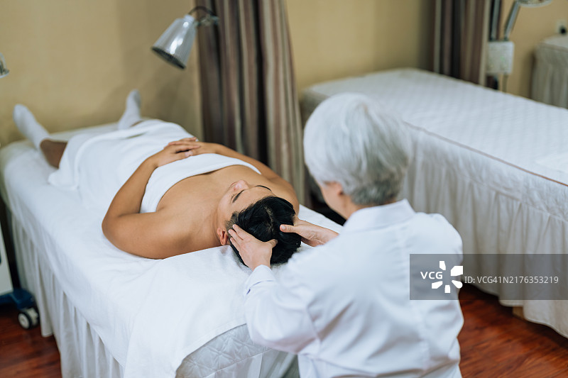 中式按摩：年长的中医女医生为年轻男运动员进行按摩图片素材