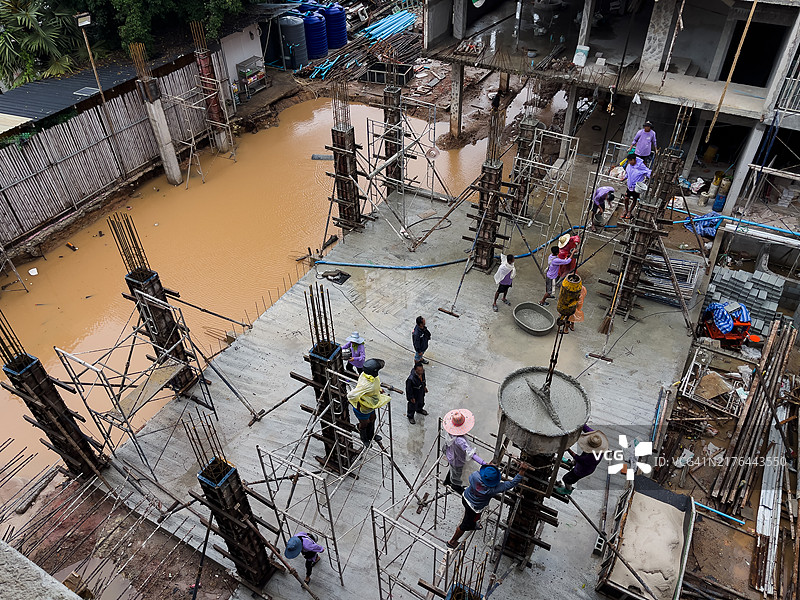 建筑工人在被洪水淹没的建筑工地上加固混凝土柱的鸟瞰图，可以看到积水和脚手架图片素材