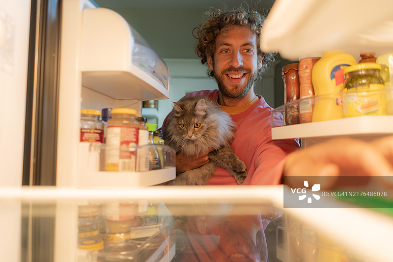 男人抱着猫看着冰箱图片素材