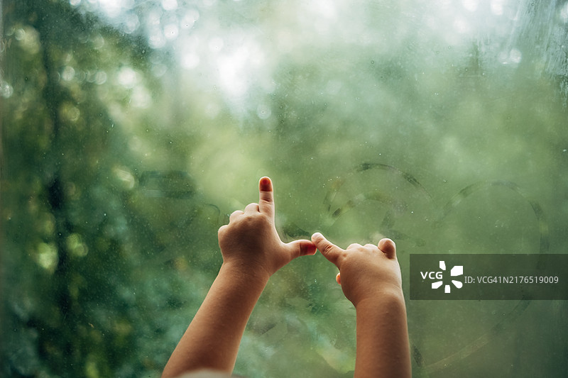 儿童在雾气蒙蒙的窗户上画一个心，手部特写图片素材