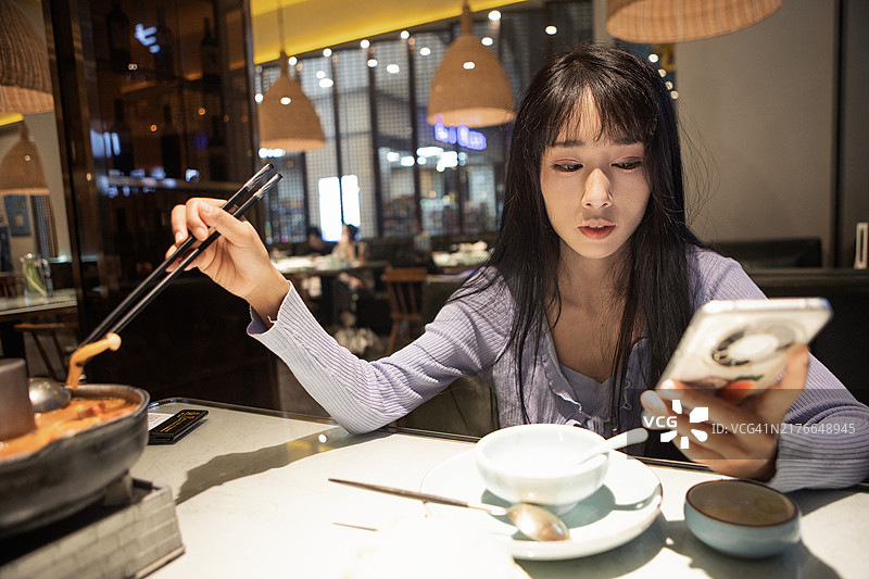 亚洲女性边吃东西边看手机图片素材