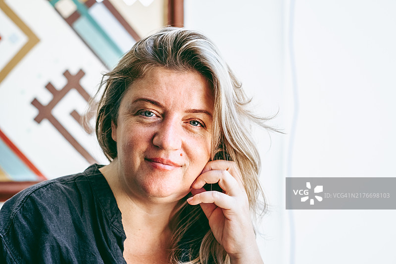 自然亲密的特写肖像，描绘一位浅金色头发的女性，温柔地微笑着直视镜头，室内拍摄。图片素材