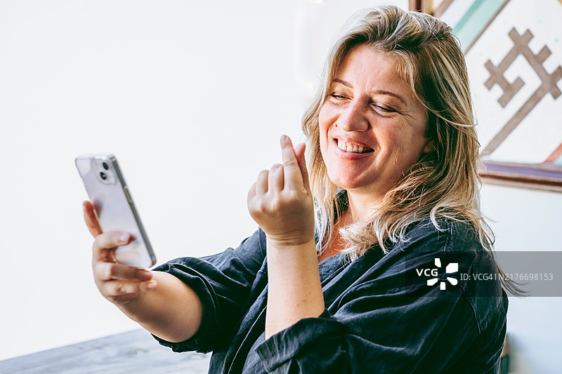 微笑的女人用智能手机享受视频通话，做心形手势图片素材