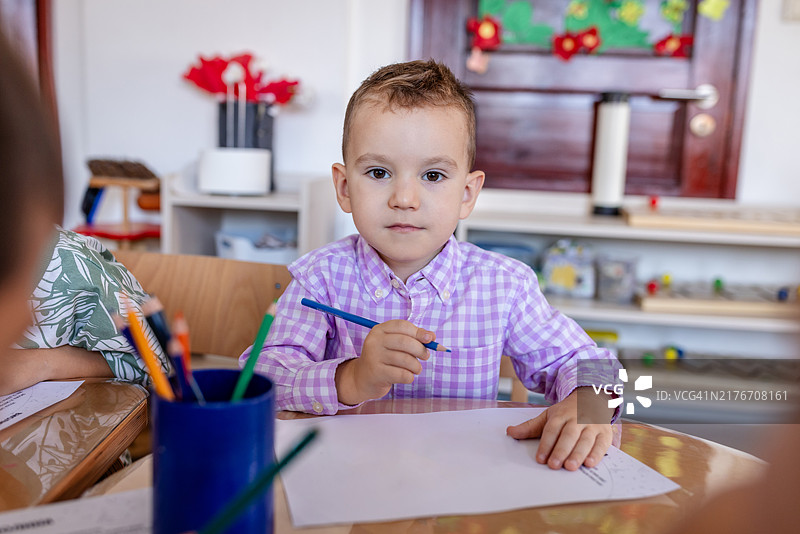 穿着格子衬衫在热闹的课堂上进行艺术创作的男孩图片素材