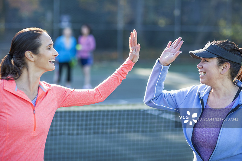 年长的白人女性与在户外球场上打网球的女性击掌图片素材