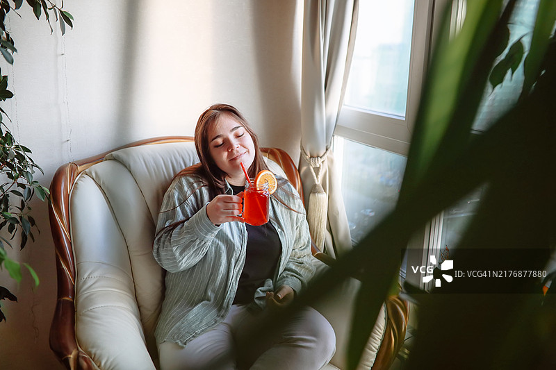 居家鸡尾酒时光：女人在家舒适地享用橙片红色水果饮品图片素材