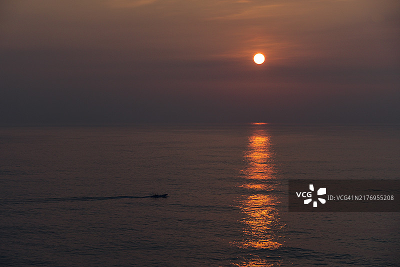 日出时分的花莲七星潭，阳光洒在海面上，将海面染成橙红色，一艘渔船缓缓驶过平静的海面图片素材
