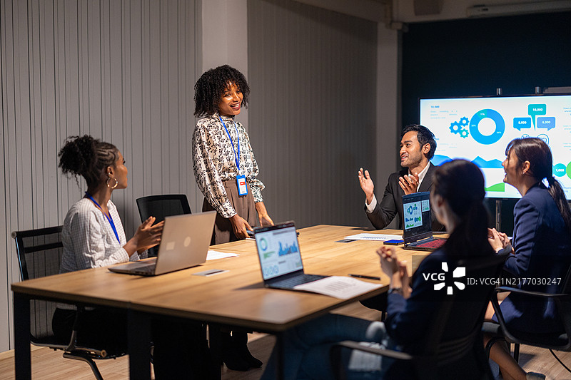 繁忙的会议室内部：一位专业的非洲裔女性在同事的掌声中进行领导力演讲，体现了多样性、团队合作和成功的企业合作图片素材