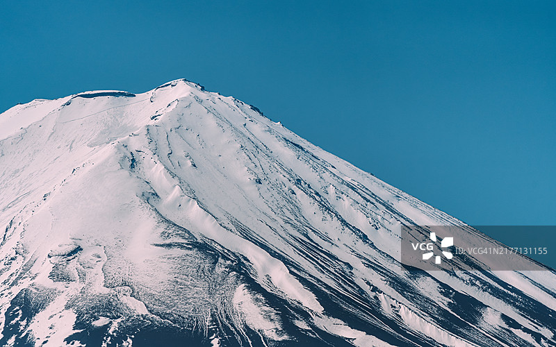 从日本山梨县青木原森林俯瞰富士山的日出。清晨的阳光将覆盖着雪的山顶沐浴在柔和的粉色光芒中，而下面浓密而阴暗的森林则突显了山的雄伟气势。图片素材
