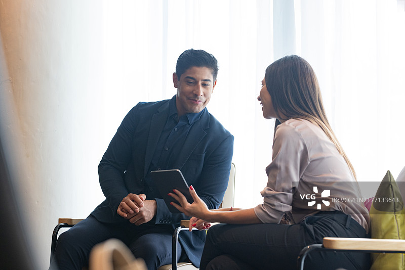两位拉丁裔千禧一代的商务人士穿着智能休闲服装坐在办公室交谈。图片素材
