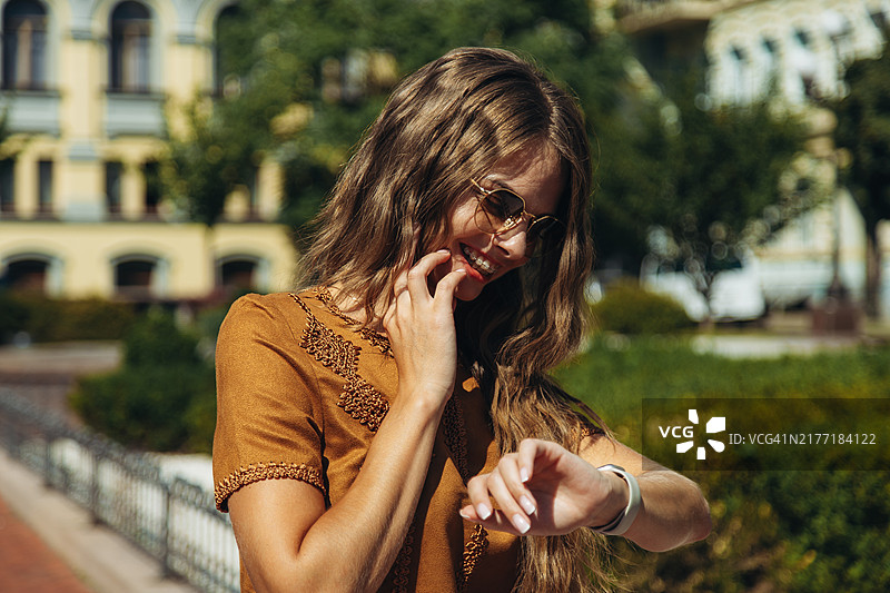 在阳光明媚的公园里，戴着太阳镜的年轻女子看着手表图片素材