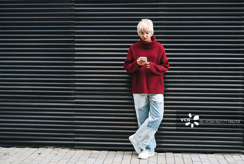 戴眼镜短发少女在城市街道墙边使用手机图片素材