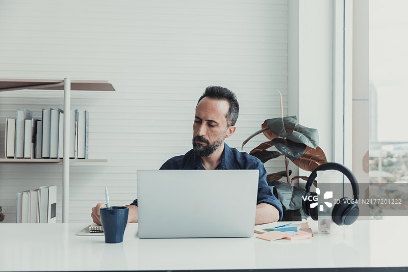 一个专注的男人在明亮的办公室环境中，白天在现代桌子上使用笔记本电脑工作图片素材