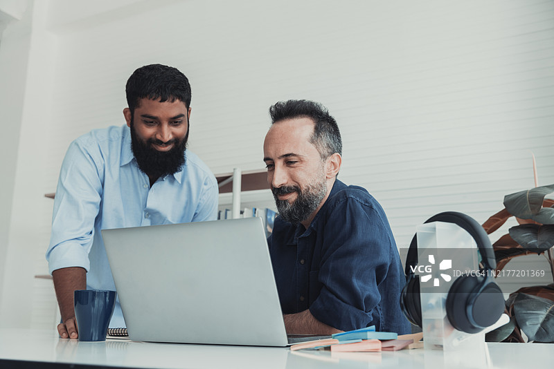 两位专业人士在现代办公室环境中协作，桌上有一台笔记本电脑。图片素材