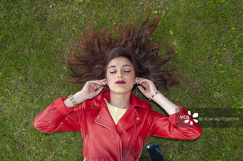 戴着无线耳机躺在草地上的女人图片素材