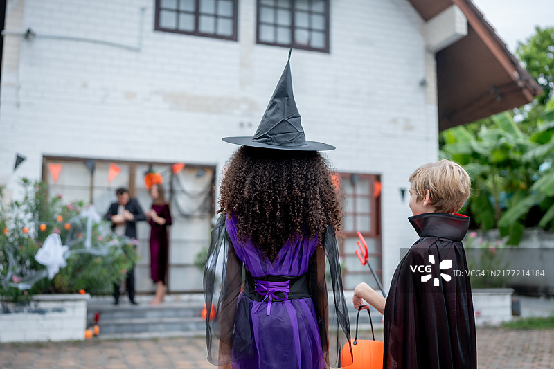 多种族儿童在家里一起庆祝万圣节派对。可爱的孩子穿着万圣节服装，拿着不给糖就捣蛋的南瓜篮，在家里节日期间接受糖果图片素材