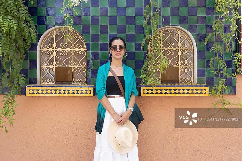 年轻的菲律宾女性站在摩洛哥马拉喀什的马约雷尔花园外，装饰性窗户和悬挂植物前。图片素材