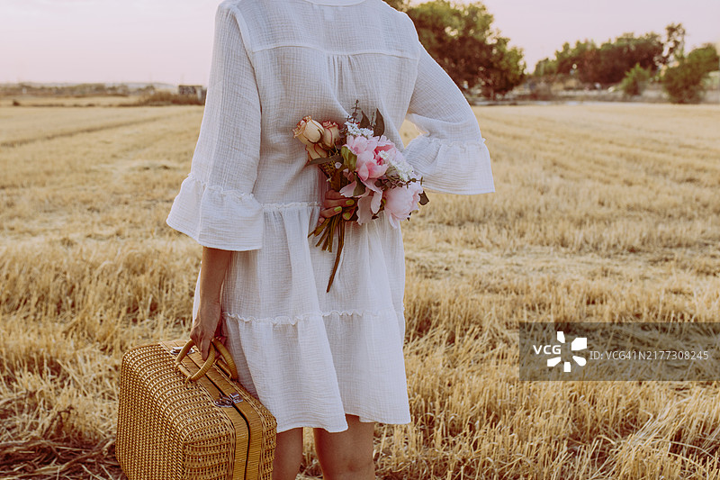 拿着柳条野餐篮的西班牙裔女人走在秋日日落时分的玉米地里，站在麦田里图片素材