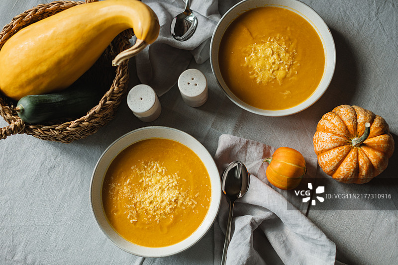 俯视图显示两碗自制南瓜汤，上面撒有帕尔马干酪，桌上还有新鲜的南瓜。图片素材