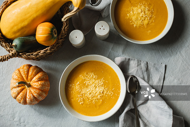 俯视图显示两碗自制南瓜汤，上面撒有帕尔马干酪，桌上还有新鲜的南瓜。图片素材
