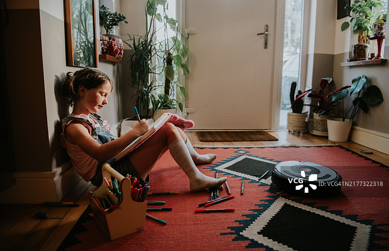 孩子用彩色笔在笔记本上绘画，扫地机器人在清洁地毯图片素材