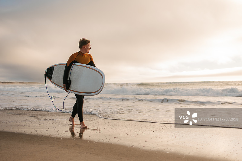 日落时分在海边行走的冲浪者图片素材
