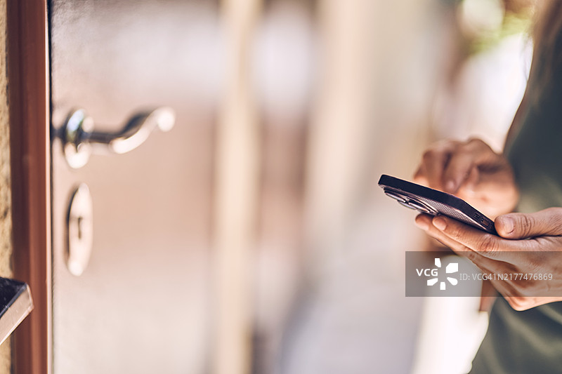 女人拿着手机打开门。手持智能手机与入口。图片素材