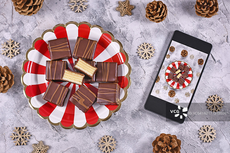 美食摄影概念：德国分层冬季蛋糕果仁糖（Baumkuchen）放在盘子里，旁边是拍摄食物照片的手机图片素材