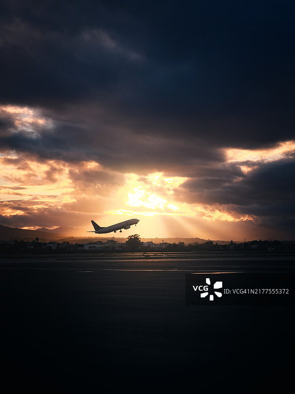 飞机在多云的天空和日落时分过滤的阳光中起飞图片素材