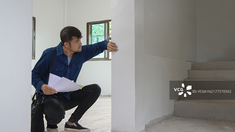 用手敲击房屋墙壁以检查房屋强度的亚洲男人。首次购房和测试房屋结构强度的概念图片素材