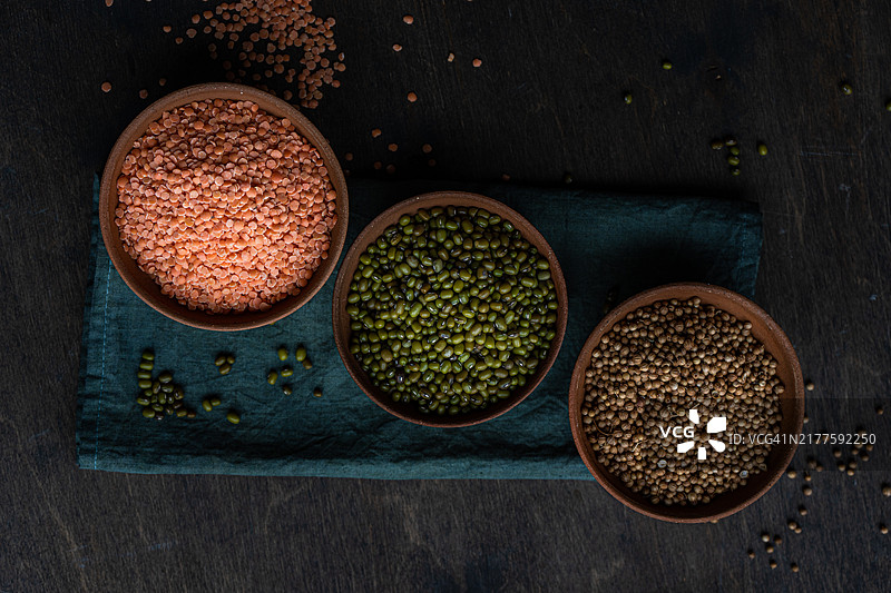 俯视：木桌上餐巾上的三碗红扁豆、芫荽籽和绿豆图片素材