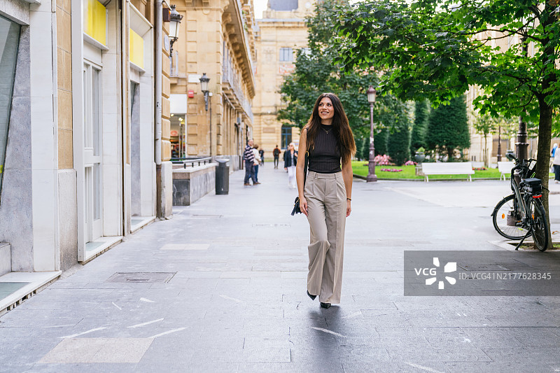 快乐的年轻女子在阳光明媚的日子里漫步于迷人的城市街道图片素材