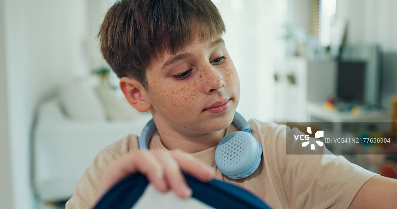 男孩在家整理上学用的书包，戴着耳机，专注于准备和责任。图片素材