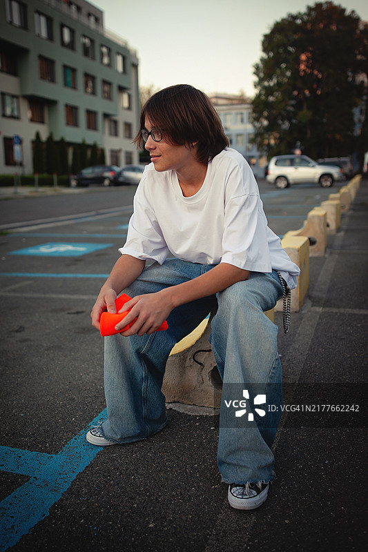 青少年男孩肖像：白色T恤、宽松牛仔裤、橙色无檐小便帽和裤链；青年文化、时尚潮流、当代美学图片素材