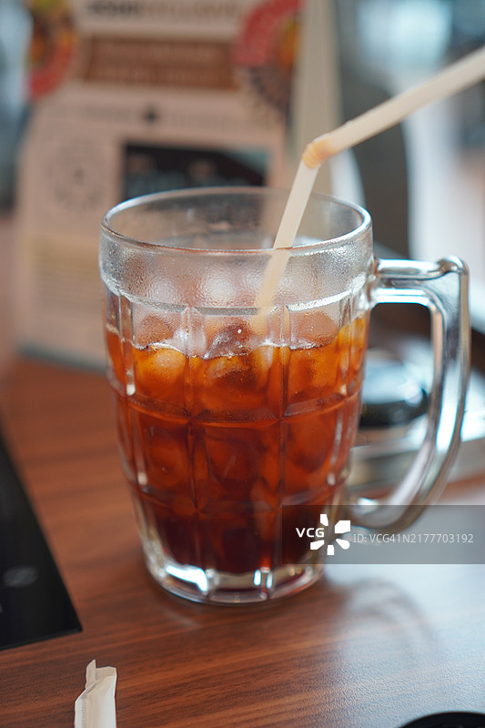 清澈的水中盛着黑冰茶，放在木桌上。饮品图片素材
