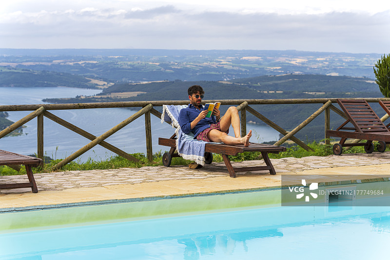 男人在山坡上的泳池边阅读图片素材