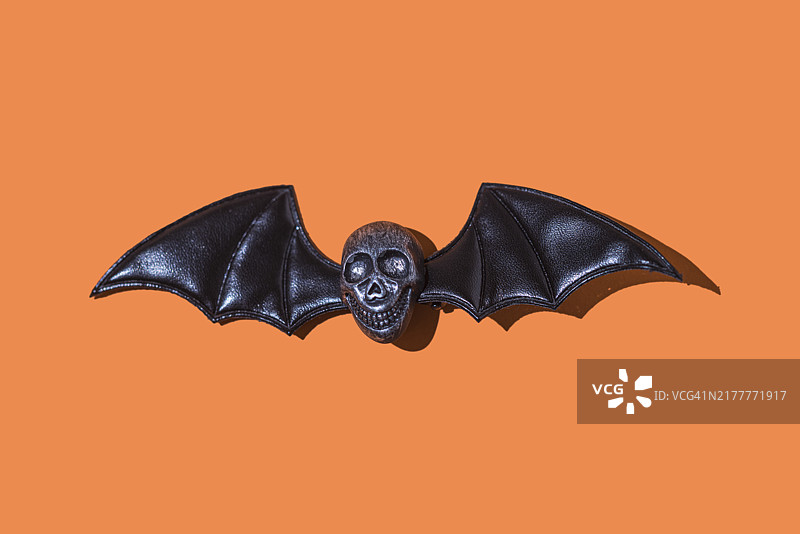 橙色背景上的一排蝙蝠翅膀金属骷髅头，万圣节概念图片素材