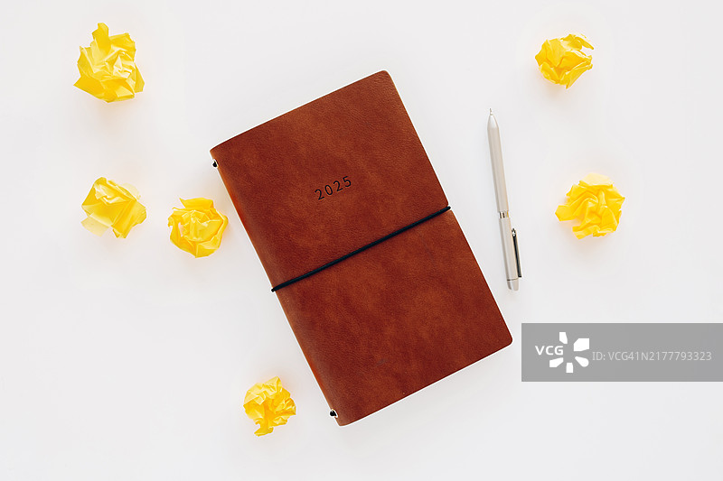2025年计划本、钢笔和皱巴巴的纸球在白色背景上图片素材