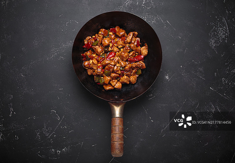 黑色背景下的炒锅中的传统中式菜肴宫保鸡丁图片素材