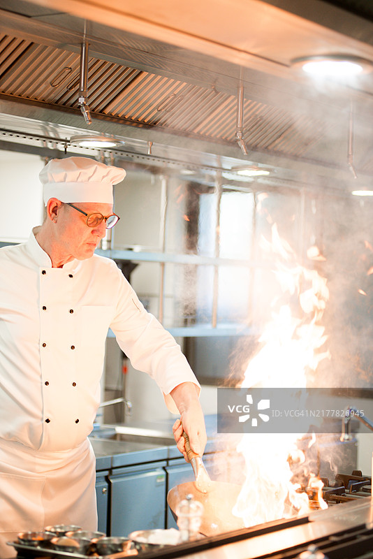 白人厨师的手紧握锅柄，厨师用手提起锅，熟练的技巧，翻炒米饭时火焰激烈，燃气灶上火焰炽热。锅因厨师的技巧而四处冒烟。图片素材