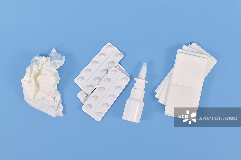 蓝色背景上的鼻腔喷雾剂、药丸和用过的纸巾俯视图图片素材